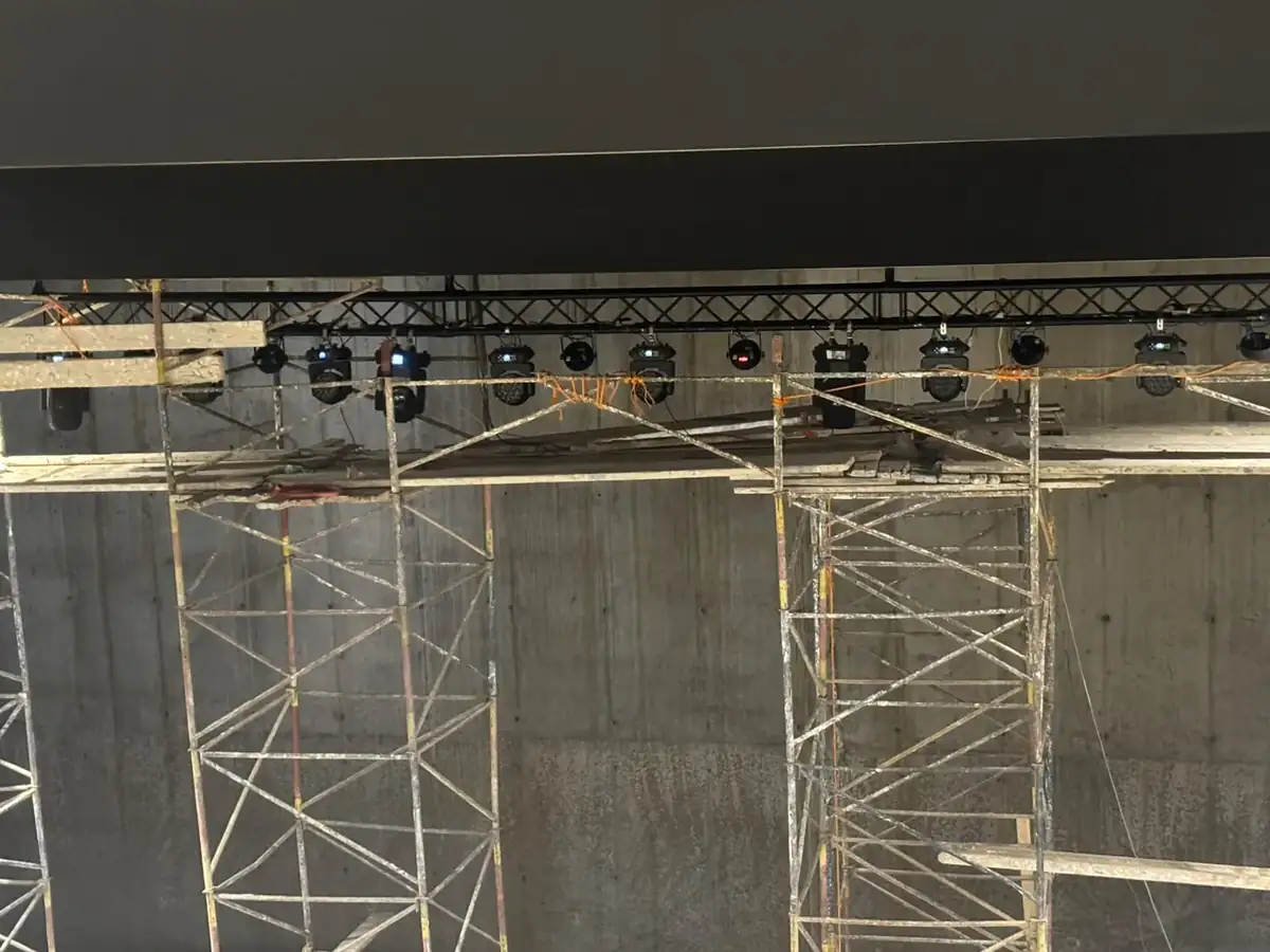 Pont en truss noir équipé de lyres wash et de projecteurs au-dessus de la scène, échafaudages en place